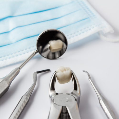 Tooth extraction concept with an array of stainless steel dental tools and a mask with the extracted tooth clasped in the pincers and reflected in the mirror